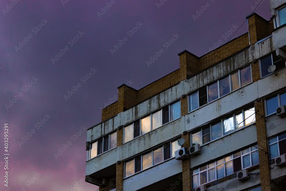 Windows of an old brick apartment building against the backdrop of a colorful sunset purple sky