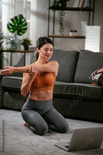 Fototapeta Naklejka Na Ścianę i Meble -  Athletic woman in sportswear doing stretching exercises at home in the living room. Fit woman training at home.