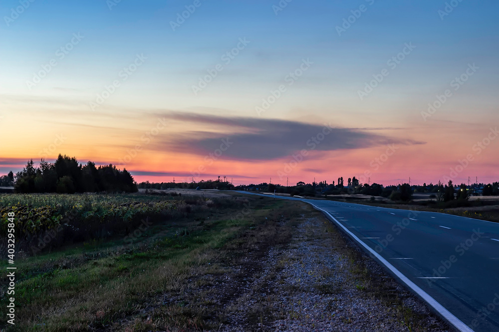 Intercity road outside the city at sunset. Village in the background and forest.
