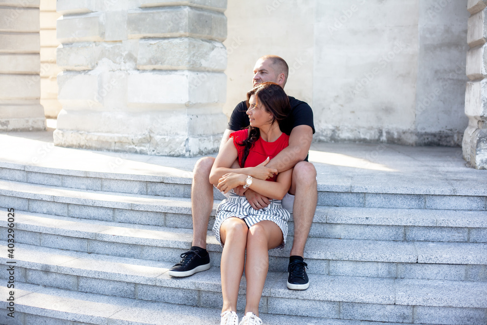 Man and woman hugging, laughing and have fun outdoor in the street of the city. People in relationship sit on the stairs