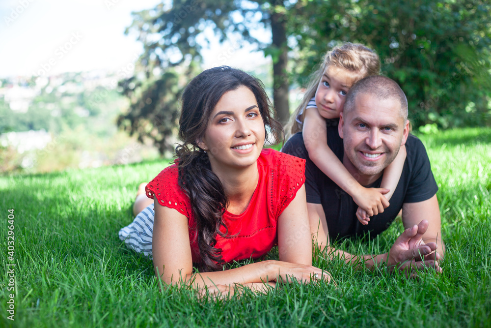 Obraz premium happy parents with daughter lies on the green grass. People having fun on the park. Woman and kid hug the father