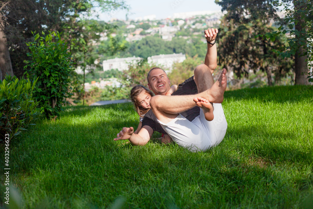 Happy family laughing in green grass of the park. Father plays with daughter. People have fun Happy family laughing in green grass of the park. Father plays with daughter. People have fun