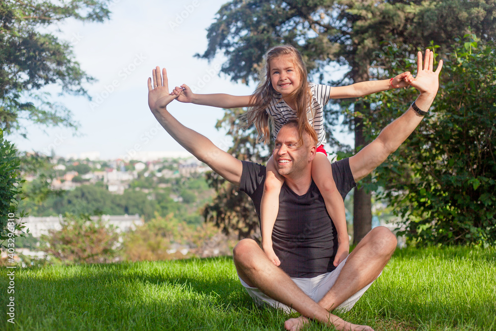 Happy family laughing in green grass of the park. Father plays with daughter. People have fun Happy family laughing in green grass of the park. Father plays with daughter. People have fun