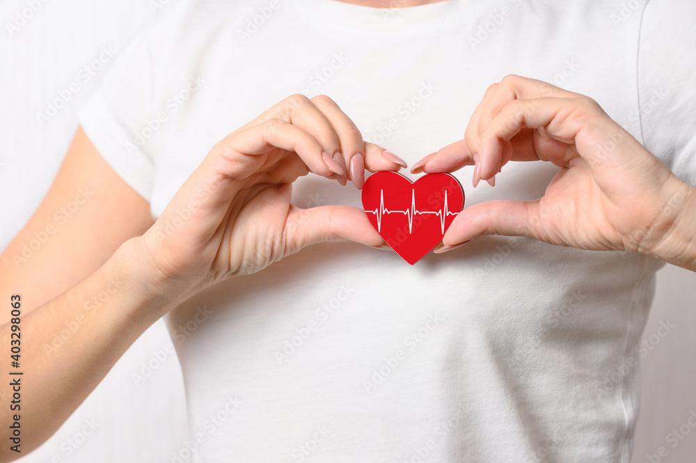 The girl is holding a red heart with a white pulse line on her chest. Cardiac disease treatment concept. A healthy pulse with a healthy lifestyle. The girl is holding a red heart with a white pulse line on her chest. Cardiac disease treatment concept. A healthy pulse with a healthy lifestyle.