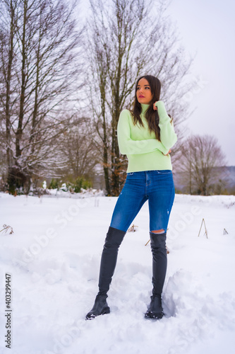 Winter lifestyle, portrait young pretty brunette Caucasian woman in green outfit and jeans, smiling in the snow, vacation in nature