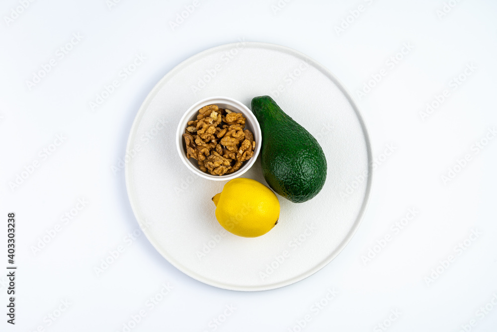 Avocado and lemon and walnuts in a white flat plate. Top view with space to copy. The concept of healthy eating. Avocado and lemon and walnuts in a white flat plate. Top view with space to copy. The concept of healthy eating.