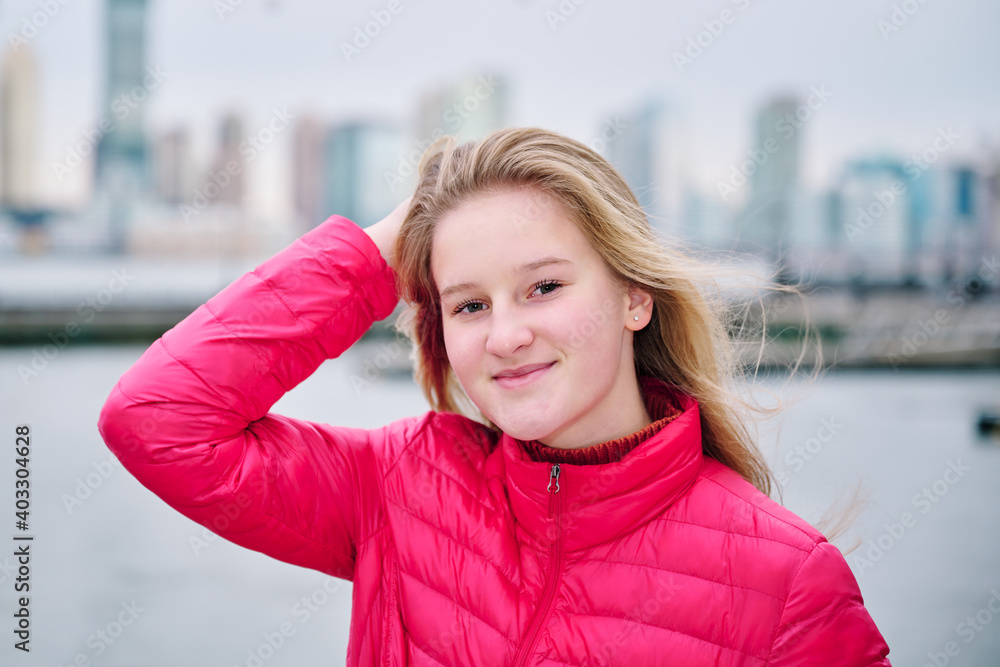 A pretty teenager is wearing a pink puffy coat and looks cosy and warm. She looks happy, has long fair hair and white skin with rosy cheeks and green eyes. The New York Skyline is in the background. A pretty teenager is wearing a pink puffy coat and looks cosy and warm. She looks happy, has long fair hair and white skin with rosy cheeks and green eyes. The New York Skyline is in the background.