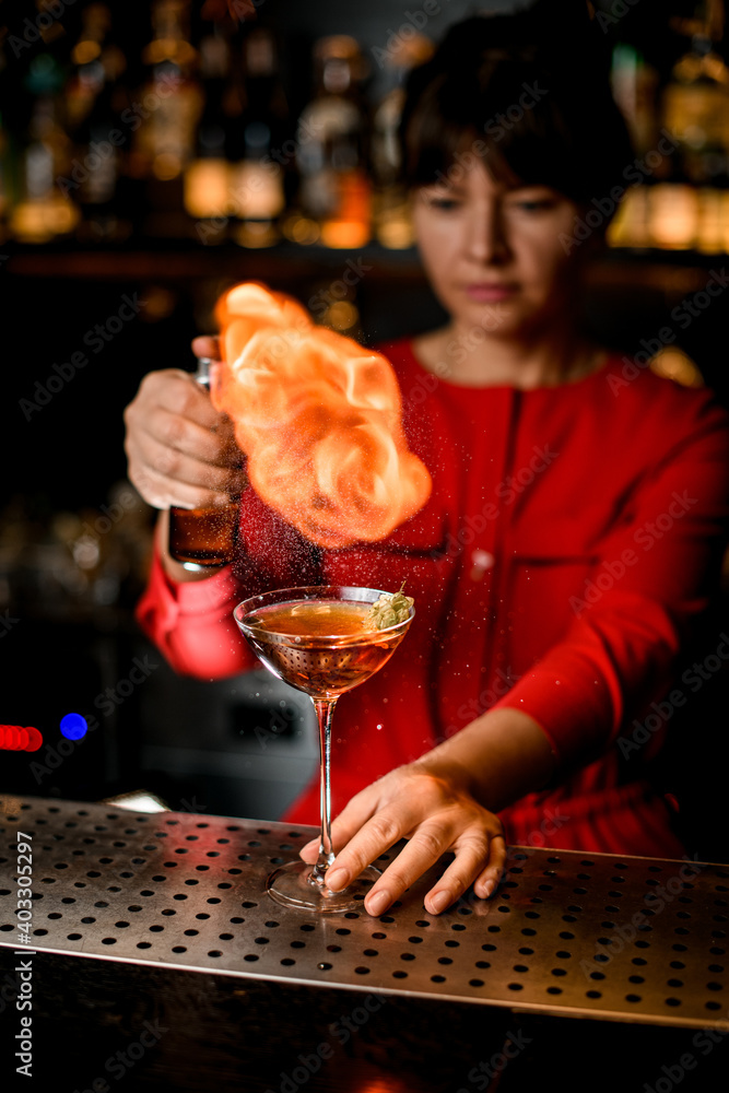 wineglass with alcoholic beverage stands on bar counter and woman makes fire flame over it