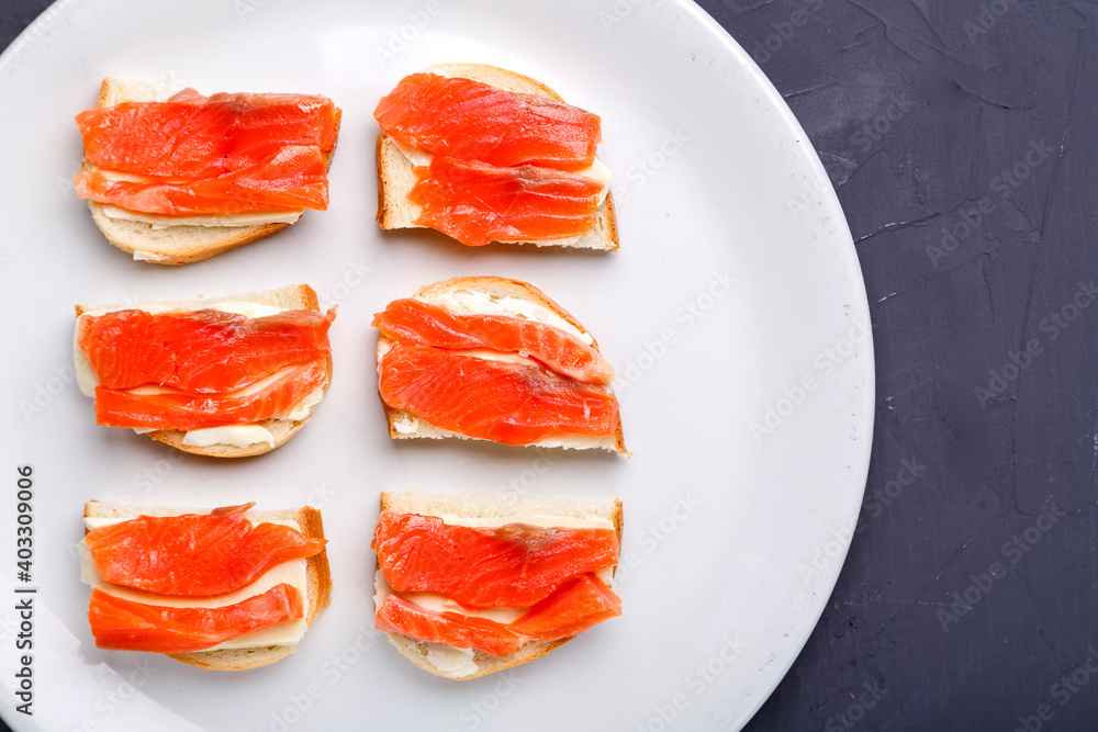 Bruschettes with butter and trout on a white plate on a gray background. Bruschettes with butter and trout on a white plate on a gray background.