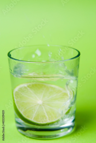 Limettenscheibe im Wasserglas vor grünem Hintergrund