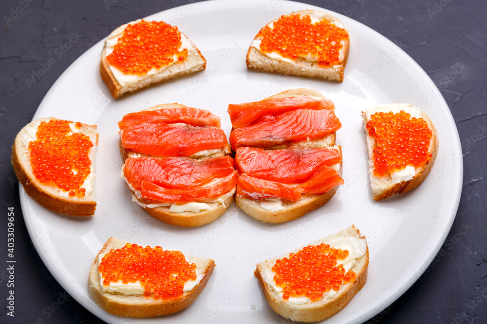 Bruschettes with butter and red caviar and trout on a white plate. Bruschettes with butter and red caviar and trout on a white plate.