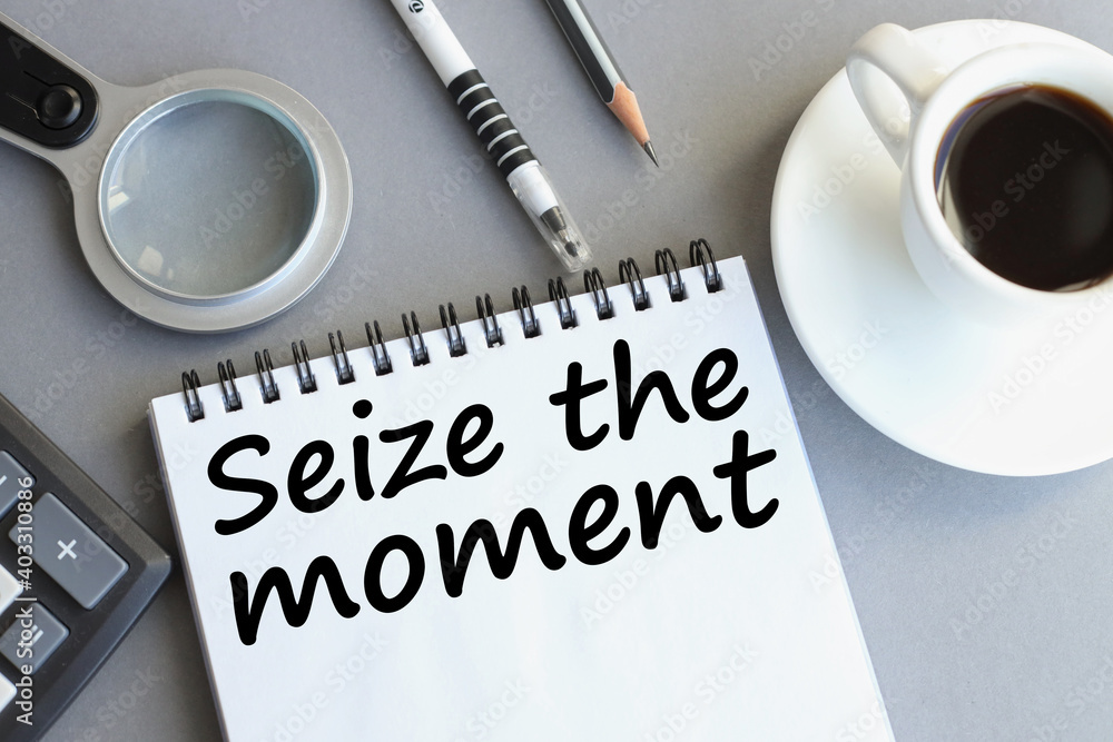SEIZE THE MOMENT. text in notebook on gray background near magnifier, calculator. business concept SEIZE THE MOMENT. text in notebook on gray background near magnifier, calculator. business concept