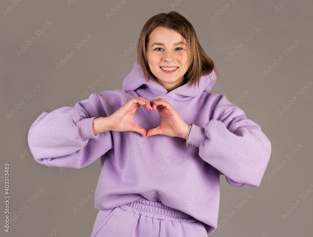 Pretty romantic young woman making a heart gesture with her fingers in front of her chest showing her love and affection with a happy tender smile Pretty romantic young woman making a heart gesture with her fingers in front of her chest showing her love and affection with a happy tender smile