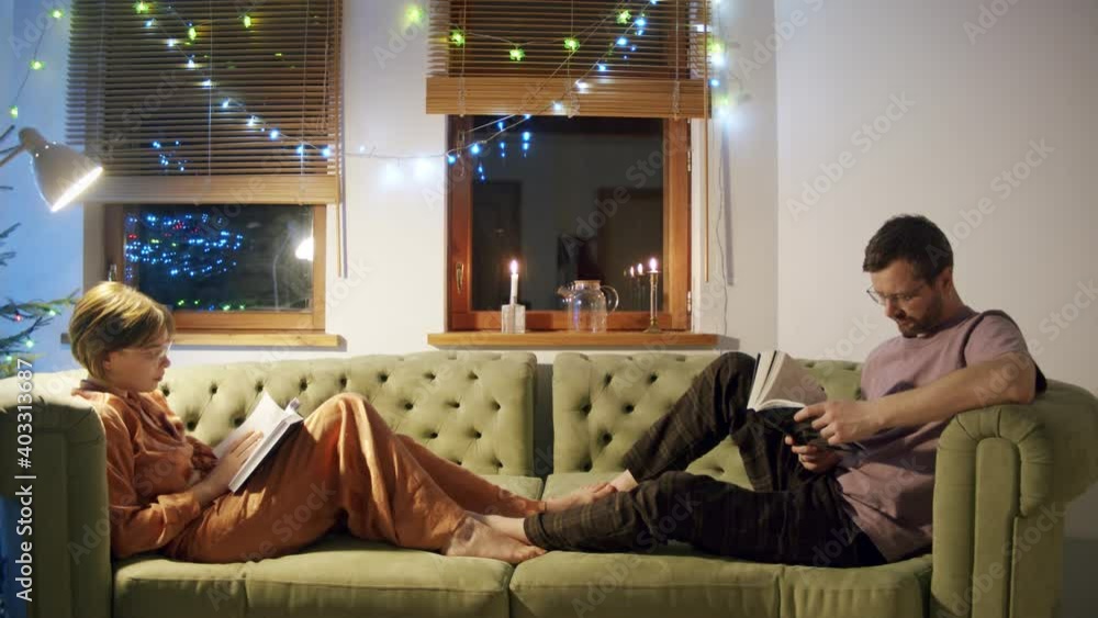 a man and a woman a married couple comfortably sitting reading books lying on the couch during the New Year and Christmas holidays. a man and a woman a married couple comfortably sitting reading books lying on the couch during the New Year and Christmas holidays.