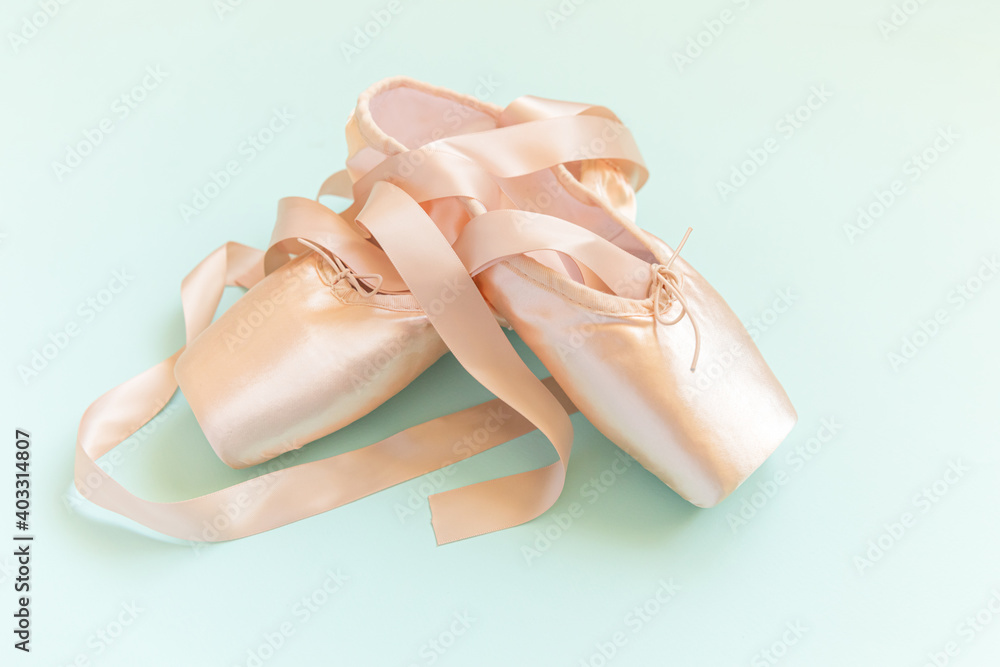 New pastel beige ballet shoes with satin ribbon isolated on blue background. Ballerina classical pointe shoes for dance training. Ballet school concept. Top view flat lay, copy space New pastel beige ballet shoes with satin ribbon isolated on blue background. Ballerina classical pointe shoes for dance training. Ballet school concept. Top view flat lay, copy space