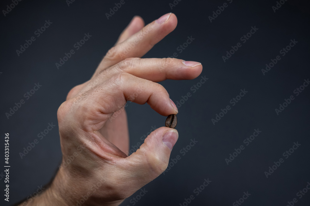 male hand is holding a coffee bean over dark background