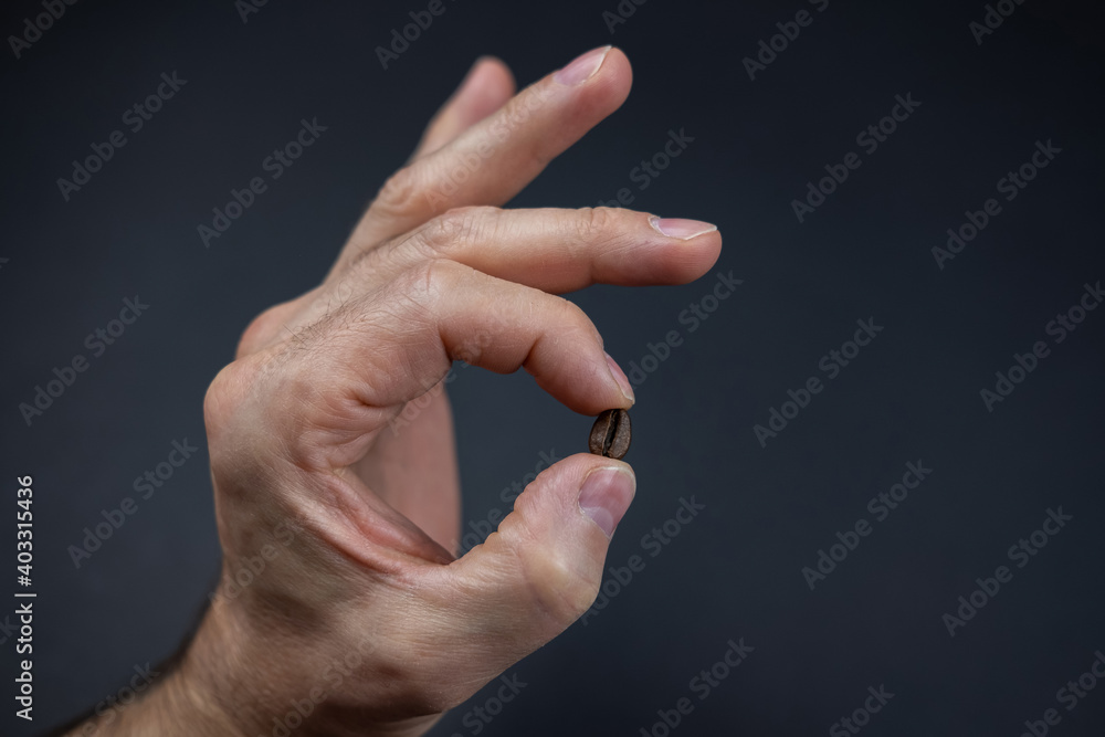 male hand is holding a coffee bean over dark background male hand is holding a coffee bean over dark background