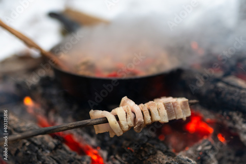 Lard cooking on stick over fire in winter forest camp