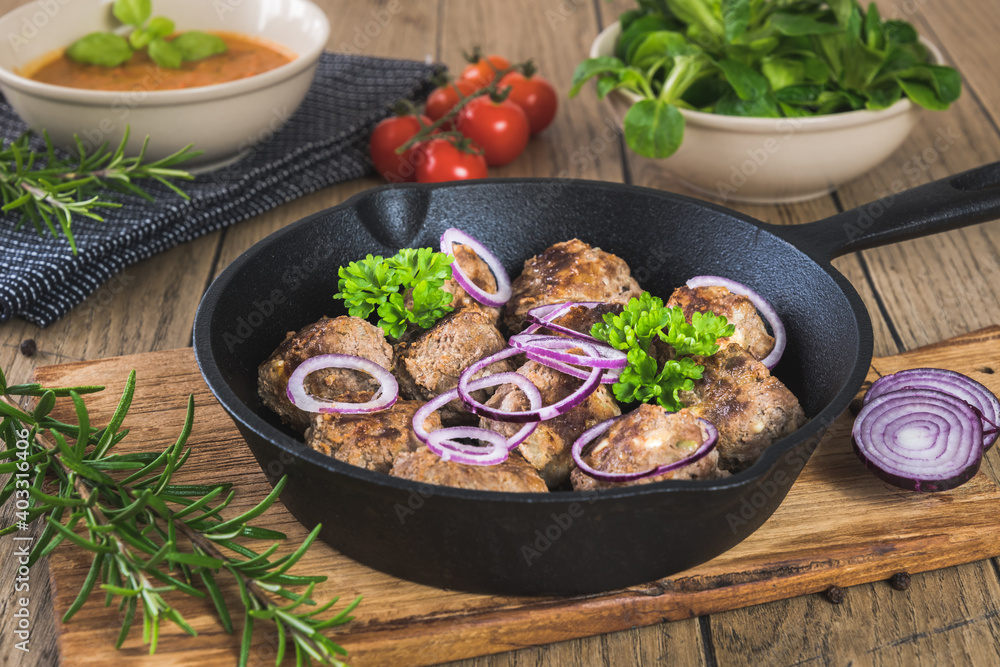 Meatballs with feta cheese in a cast-iron pan on a rustic wooden table