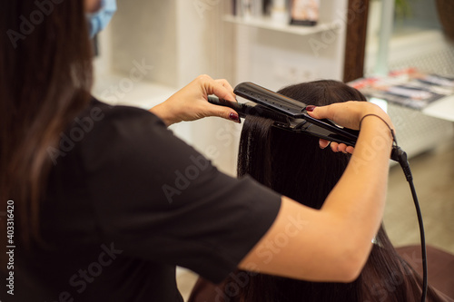 Close up image of unrecognizable hairdresser in black uniform while making a hairstyle using a hair straightener