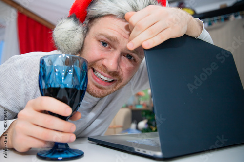 Young happy man having video call via laptop with wine, celebrating Christmas alone at home