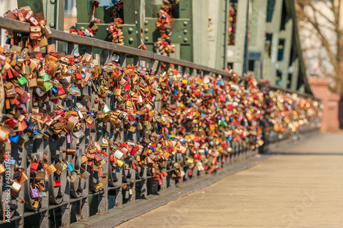 Many locks on the green bridge railing of the iron bridge in Frankfurt over the river Main. Locks of love in different colors in sunshine with blurry background