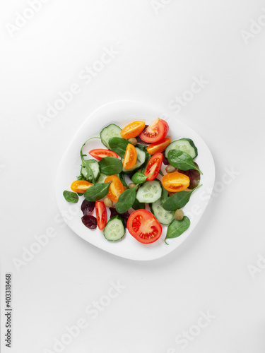 White plate with a bright fresh vegetable salad of vegetables and greens on a light background