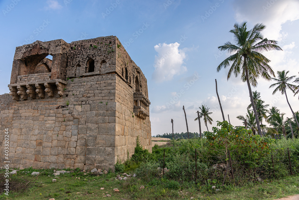 Hampi, Karnataka, India - November 4, 2013: Gray-brown stone Mohammadan Watch tower in its setting under blue sunset sky and green palm trees, bushes and grass. 