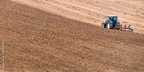 niebieski traktor z pługiem na polu