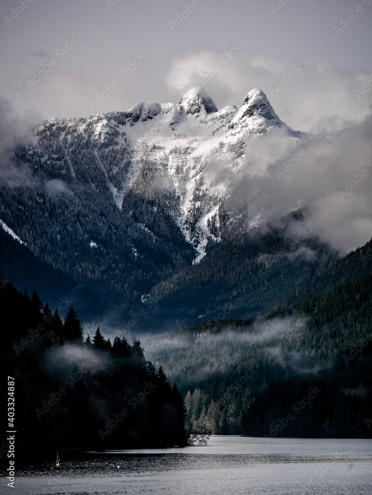 Fototapeta premium Lions peak mountain in the fog. Clouds and snow from cleveland dam and Capilano Lake