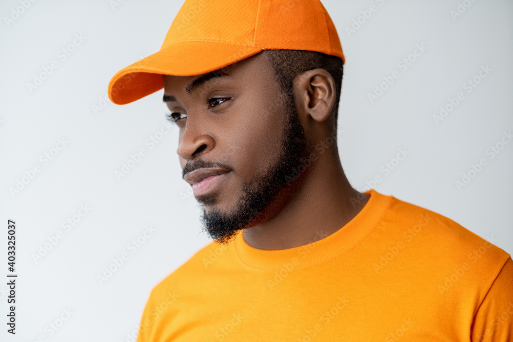 Pensive man. Attractive opportunity. Idea inspiration. Portrait of confident relaxed African guy in bright orange t-shirt matching cap thinking considering option isolated on light neutral background. Pensive man. Attractive opportunity. Idea inspiration. Portrait of confident relaxed African guy in bright orange t-shirt matching cap thinking considering option isolated on light neutral background.