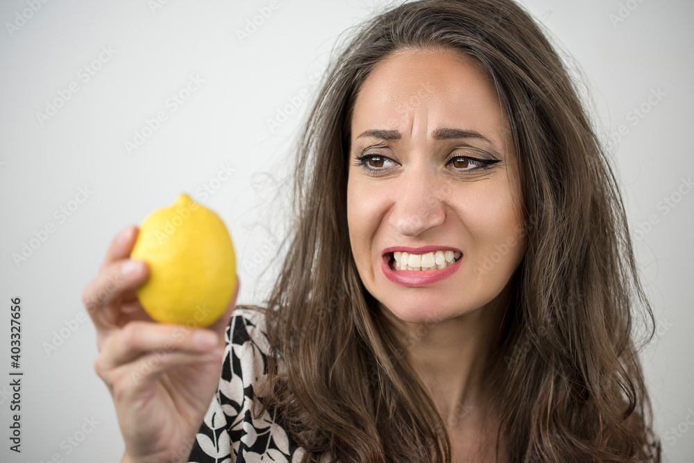 Beautiful woman is making a sour grimace while holding a lemon Beautiful woman is making a sour grimace while holding a lemon