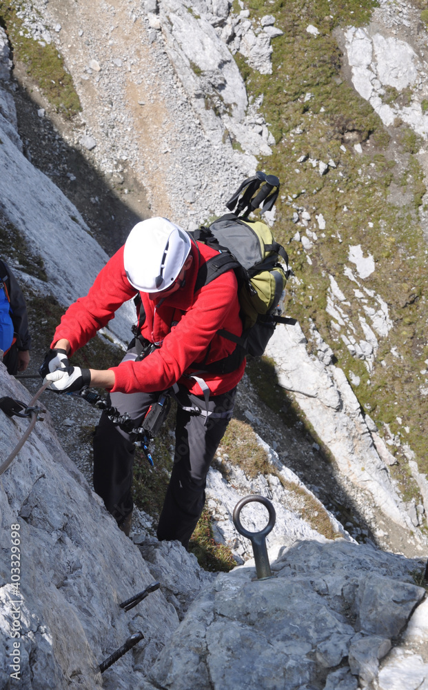 Męzczyzna w białym kasku asekuruje się na via ferracie w Dolomitach