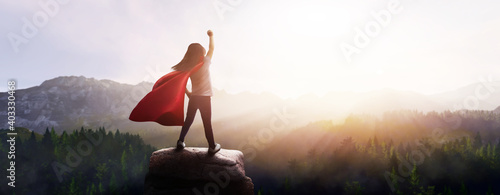 little girl dreaming of being a superhero in a beautiful mountain landscape with a raised fist photo