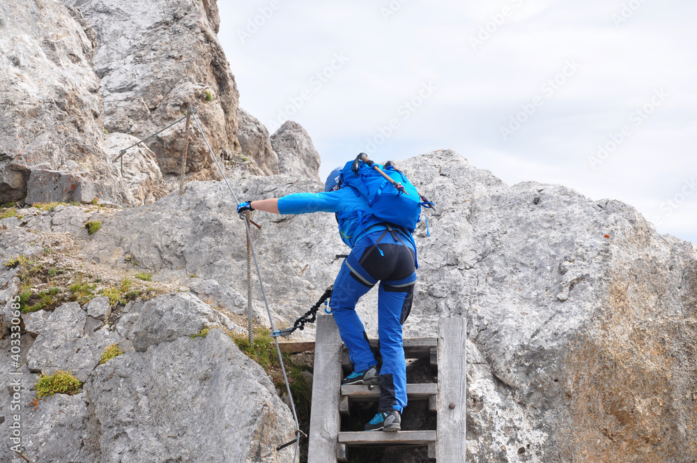 Dziewczyna w niebieskim stroju wspina sie po drabinie w Dolomitach