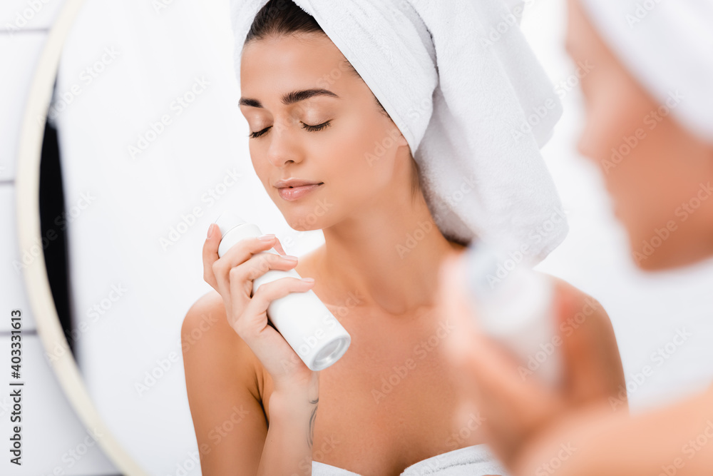 young woman with closed eyes smelling deodorant in bathroom, blurred foreground