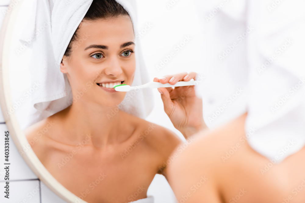young woman with white towel on head brushing teeth while looking in mirror, blurred foreground young woman with white towel on head brushing teeth while looking in mirror, blurred foreground