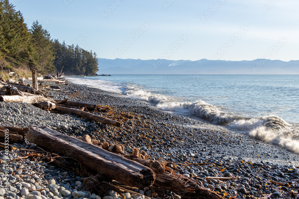 Large driftwood log and rocks on the coast with large waves breaking on the coast of the Pacific Ocean on Vancouver Island