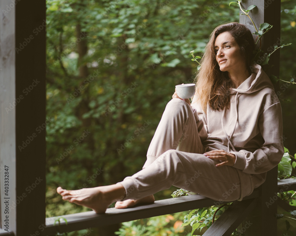 Woman in terrace with cup of coffee. Green yard. Woman in soft light costume. Summer relaxing lifestyle. Village lifestyle. Woman in terrace with cup of coffee. Green yard. Woman in soft light costume. Summer relaxing lifestyle. Village lifestyle.