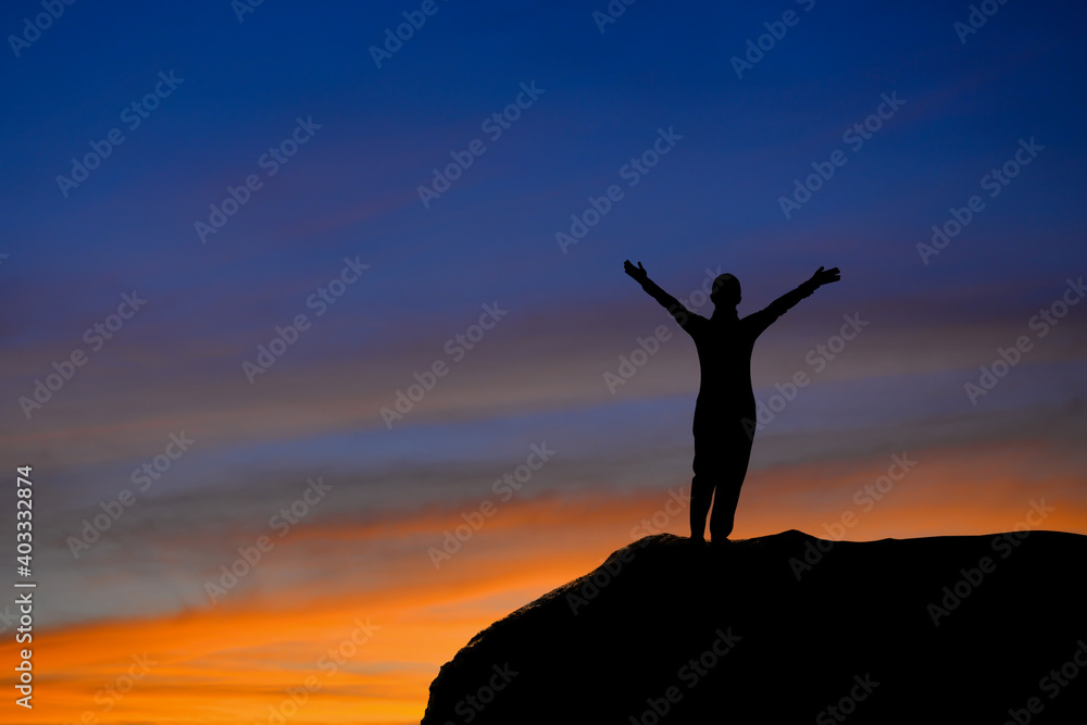 Silhouette of young female traveler standing and open arms and watched the beautiful sky and sunrise on top of the mountain. She is happy to be with herself and stay with nature at twilight time.