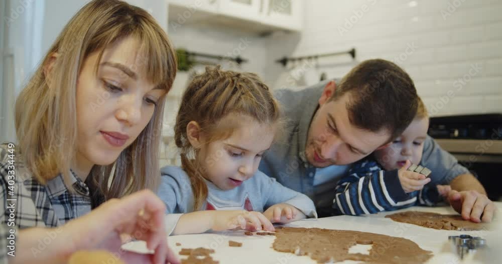 Young family spending time at home together. Parents have fun with children baking christmas cookies pastry in the kitchen. Mother and father teach their daughter and son to use cookie cutters. Young family spending time at home together. Parents have fun with children baking christmas cookies pastry in the kitchen. Mother and father teach their daughter and son to use cookie cutters.