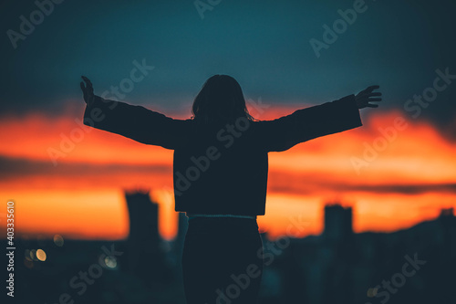 A woman raises her arms from above the city at sunset