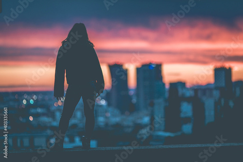 A woman looks down at the city at sunset
