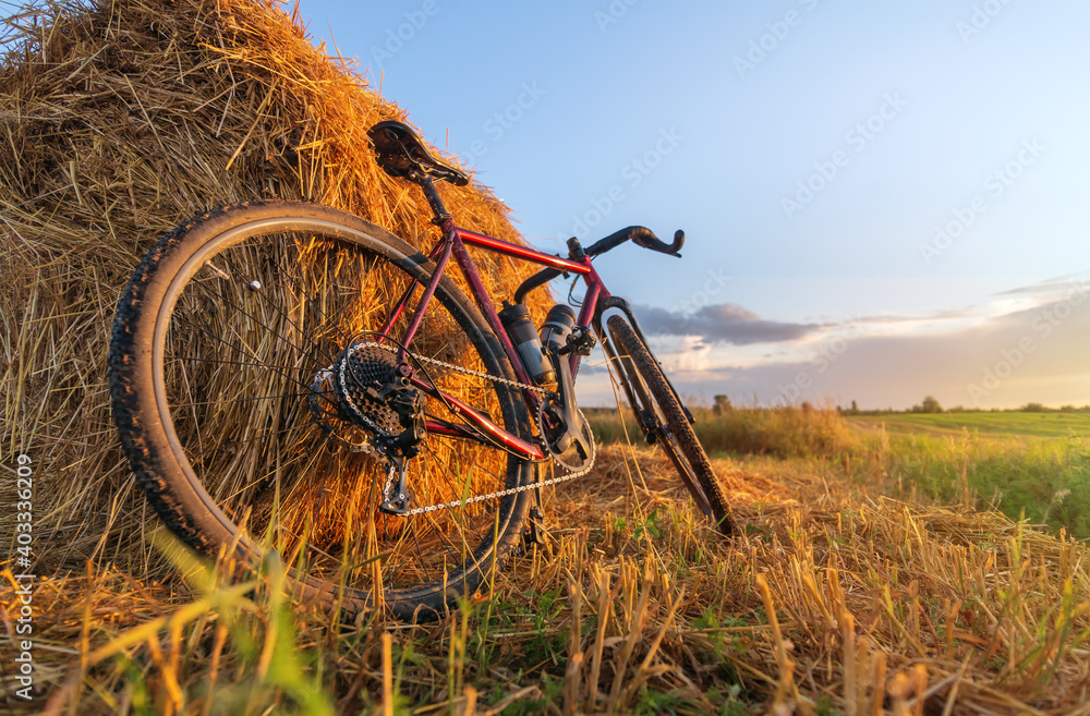 Naklejka premium Bicycle stands by haystack in a field at sunset. Low angle view.