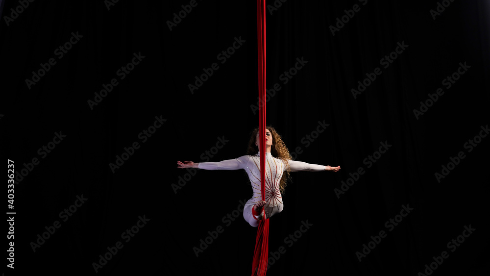 Aerial gymnast girl performs a balance trick on a split arms to the side 
