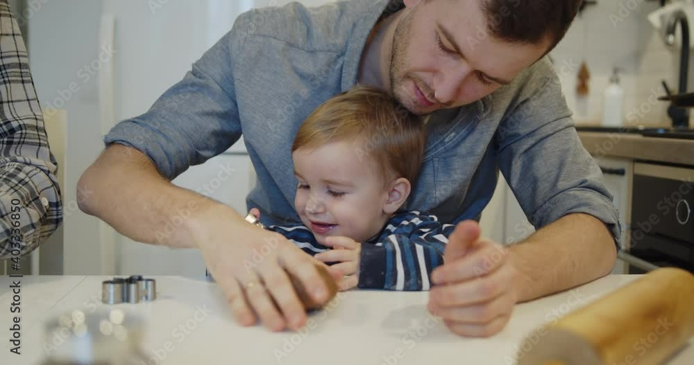 Young family spending time at home together. Father and son having fun baking cooking christmas cookies pastry in the kitchen. Loving happy father teaches cute kid to roll out the dough. Young family spending time at home together. Father and son having fun baking cooking christmas cookies pastry in the kitchen. Loving happy father teaches cute kid to roll out the dough.