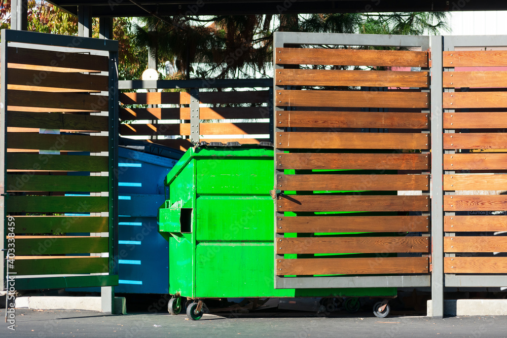 Two waste management blue and green garbage containers dumpsters in garbage enclosure used for