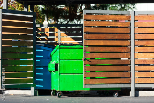 Two waste management blue and green garbage containers dumpsters in garbage enclosure used for commercial and residential garbage