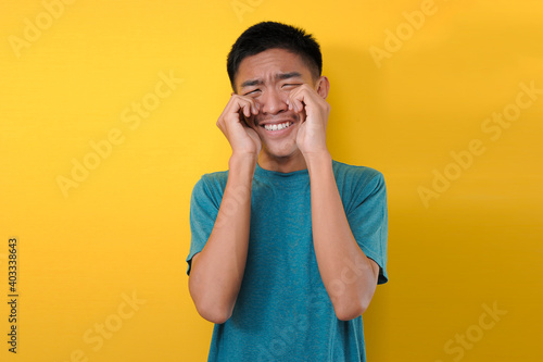 Funny and hilarious portrait of young sad asian man in overact crying gesture with hands on eyes photo