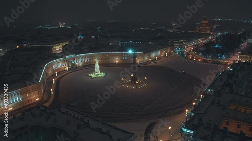 New Year's Palace Square in St. Petersburg. On the square there is a Christmas tree with lights and garlands. Snowfall, night, no people. Cars remove snow. Footage from a quadcopter. View from above. photo